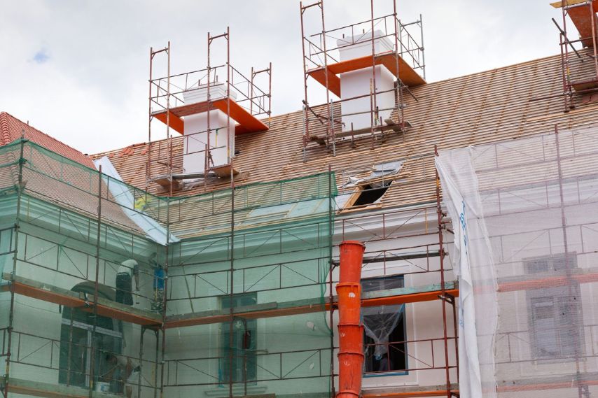 Edificio con ponteggi e rete di protezione durante i lavori di rifacimento del tetto spiovente.
